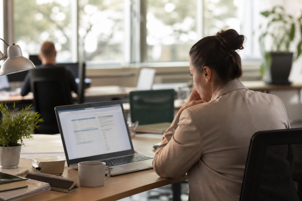 Berufserfahrene Mitarbeiterin nutzt KI auf Arbeit am Laptop in einem hellen modernen Büro und prüft konzentriert digitale Dokumente.